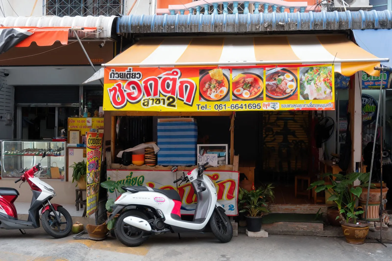 Noodle restaurant exterior in Pattaya, Thailand with vibrant signage and parked scooters.